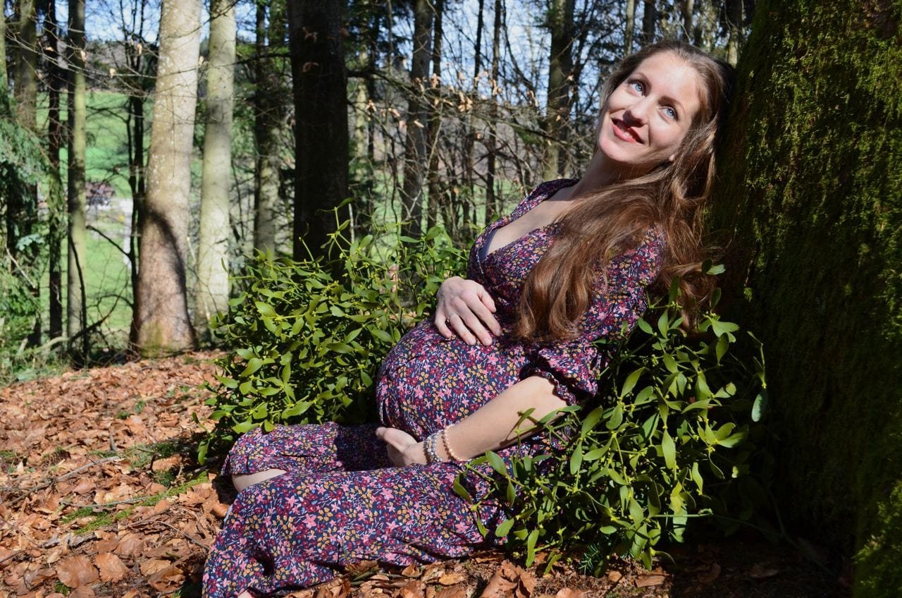 Miriam Emilia schwanger, an einen bemoosten Baum gelehnt, im sonnigen Frühlingswald